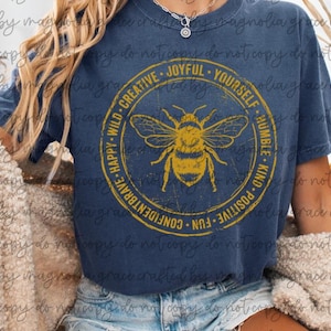 May include: Navy blue t-shirt with a yellow bee graphic inside a circle. The circle includes the words: "Happy, Wild, Creative, Joyful, Yourself, Humble, Kind, Positive, Fun, Confident, Brave." A casual, comfortable tee.