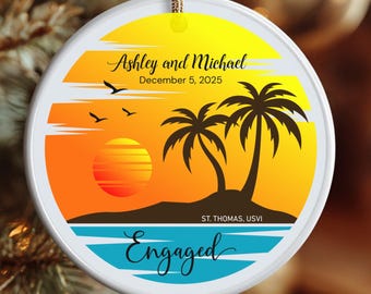 May include: A round, white Christmas ornament with a tropical sunset design. The ornament features a yellow and orange gradient sky, a setting sun, palm trees, and the words "Ashley and Michael" and "Engaged". The date "December 5, 2025" is also included.