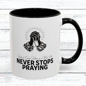 Puede incluir: Taza de cerámica blanca con interior y asa negros. La taza presenta el texto "Behind Every Soldier is a Mom Who Never Stops Praying" en negro, junto con un gráfico de manos rezando y placas de identificación.
