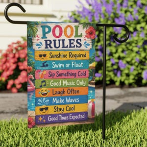 May include: A rectangular garden flag hanging on a black metal stand, featuring the text POOL RULES and eight colourful horizontal planks with icons and phrases: Sunshine Required, Swim or Float, Sip Something Cold, Good Music Only, Laugh Often, Make Waves, Stay Cool, and Good Times Expected.