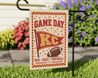 May include: A rectangular garden flag hanging on a black metal stand. The flag features a cream background with a red and gold checkered border. It displays the text GAME DAY, a red pennant with the letters KC, a football, and the text RED GOLD FOOTBALL.