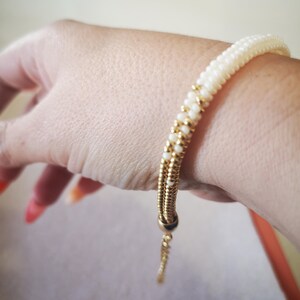 Op de afbeelding: Een witte kralen armband met een gouden ketting en een schuifsluiting. De armband is verstelbaar en kan om de pols of enkel gedragen worden.
