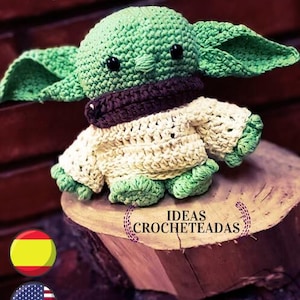 Puede incluir: Un muñeco de crochet de Baby Yoda con un suéter marrón y crema. El muñeco está sentado en un tronco de árbol con el texto "IDEAS CROCHETEADAS" en él.