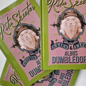 Può includere: Tre libri tascabili rosa e verdi con il titolo "The Lies & Life of Albus Dumbledore" di Rita Skeeter. I libri sono in diverse lingue: inglese, tedesco e spagnolo.