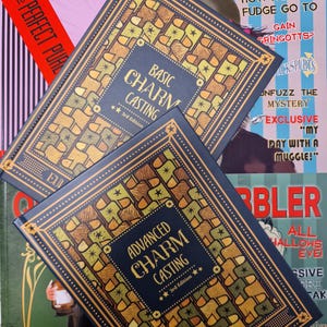 Peut inclure: Deux livres reliés en bleu avec des accents dorés et le titre "Basic Charm Casting" et "Advanced Charm Casting" sur les couvertures. Les livres sont empilés l'un sur l'autre et portent une étiquette de troisième édition en bas de la couverture.
