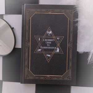 May include: A black leather-bound book with a gold embossed design. The title reads "A Beginner's Guide to Transfiguration".