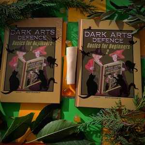 Peut inclure: Deux livres vintage intitulés "Dark Arts Defence Basics for Beginners" avec des illustrations d'enfants et de chats noirs. Les livres sont numérotés 1 et 2, avec une palette de couleurs or et crème. Le fond comprend du vert et du jaune.