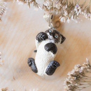May include: A white and black cat figurine with blue eyes, hanging from a silver chain. The figurine is in a curled up position, with its paws tucked under its body.