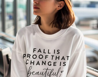 May include: White sweatshirt with the text "Fall is proof that change is beautiful" in black lettering with a small heart symbol.