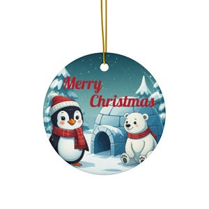 May include: Round Christmas ornament featuring a penguin and polar bear in a snowy scene. The penguin wears a red and white hat and scarf, the polar bear a red scarf. The words "Merry Christmas" are written in red.