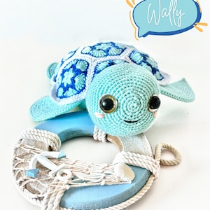 May include: A crocheted blue and white sea turtle with brown eyes, resting on a blue and white life preserver with a white anchor and rope. The text "Wally" is in a speech bubble above the turtle.