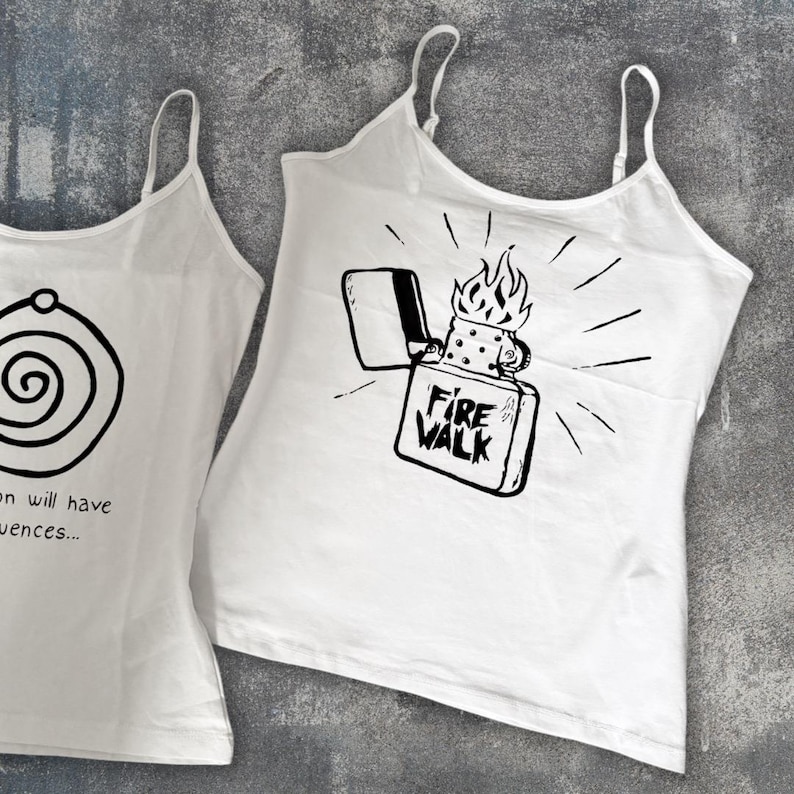 May include: Two white tank tops with thin straps. One features a black spiral design, and the other displays a black graphic of a lighter with flames and the text "FIRE WALK". The tops are made of a lightweight fabric.