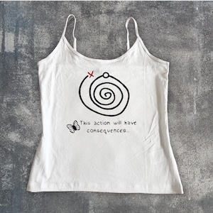 May include: White camisole top with spaghetti straps. The top features a black spiral design with a red X and the text "This action will have consequences..." along with a butterfly graphic. The top is made of a soft, lightweight fabric.