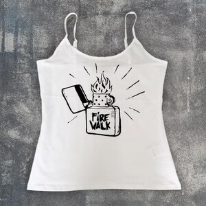 May include: White camisole top with thin straps. The front features a black graphic of a lighter with flames and the text "Fire Walk". The design includes radiating lines around the lighter.