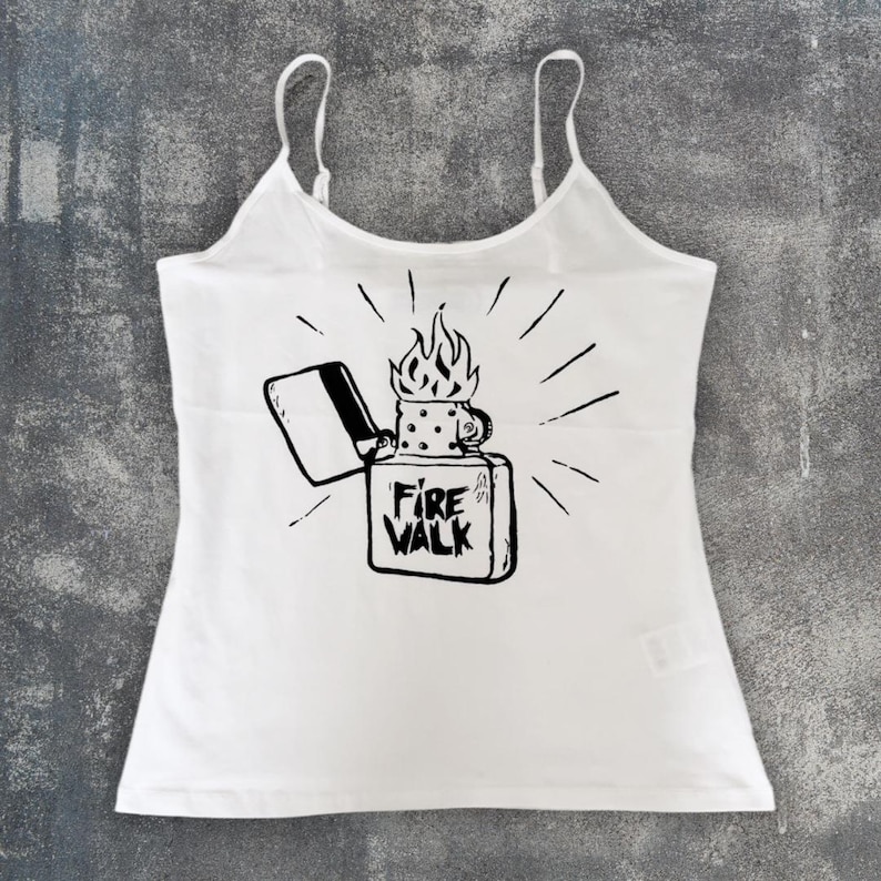May include: White camisole top with thin straps. The front features a black graphic of a lighter with flames and the text "Fire Walk". The design includes radiating lines around the lighter.