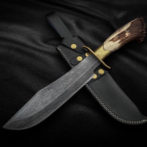 Könnte beinhalten: Ein Jagdmesser mit einem braunen Hirschhorn-Griff und einer Lederscheide. Die Klinge ist aus Stahl und hat eine strukturierte Oberfläche.