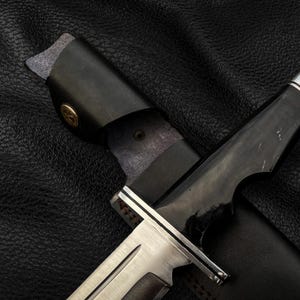 May include: A black leather sheath with a silver and black knife inside. The knife has a black handle and a silver blade.