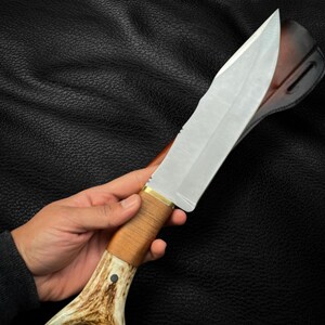 May include: A hunting knife with a brown antler handle and a leather sheath. The blade is silver and has a slight curve.