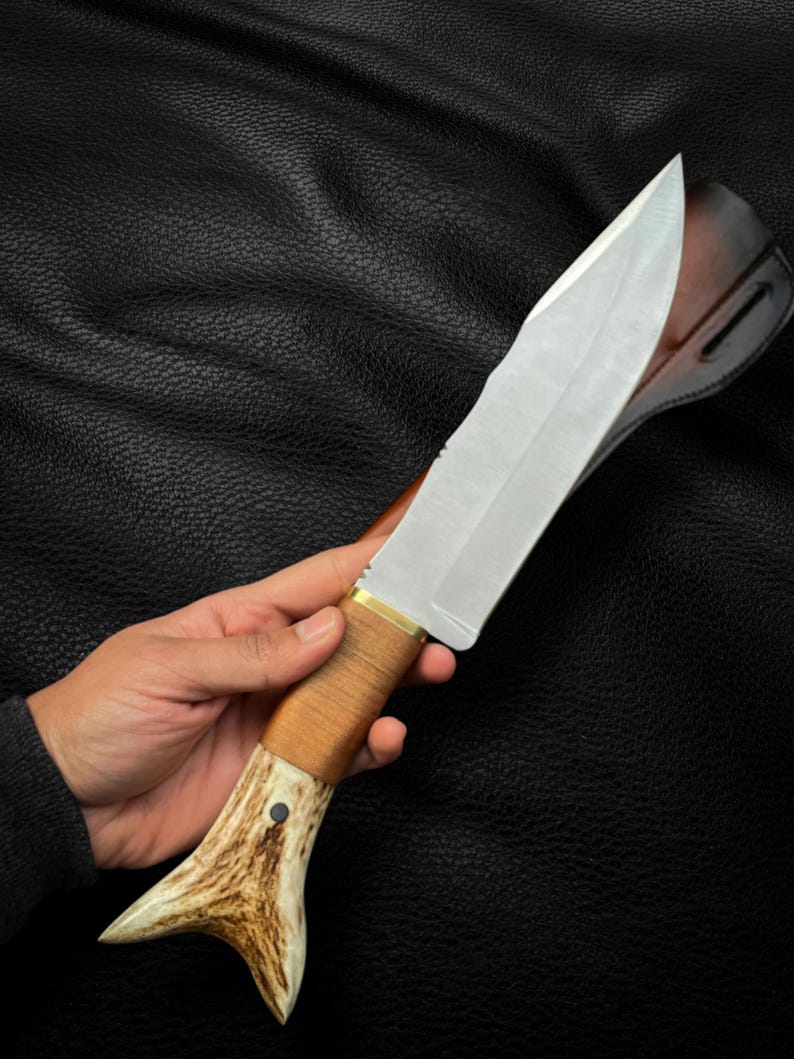 May include: A hunting knife with a brown antler handle and a leather sheath. The blade is silver and has a slight curve.