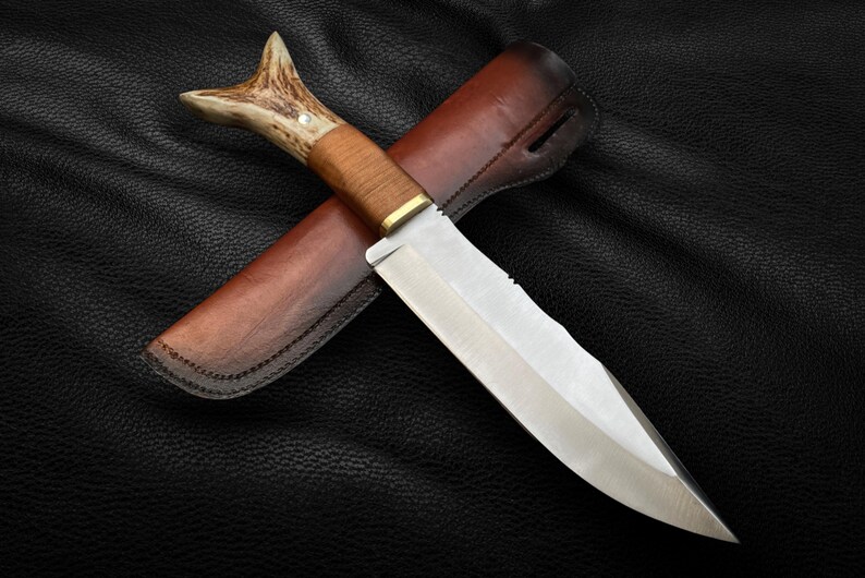 May include: A hunting knife with a brown leather sheath and a stag antler handle. The blade is silver and has a serrated edge.