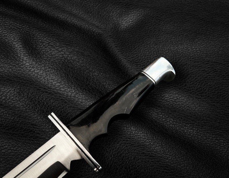May include: A black handled hunting knife with a silver blade and a black leather background.