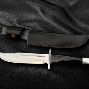 May include: A black leather sheath with a brown stitching detail and a silver-colored knife with a black handle.