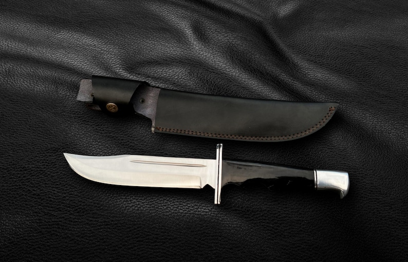 May include: A black leather sheath with a brown stitching detail and a silver-colored knife with a black handle.