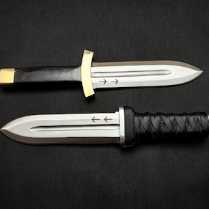 May include: Two daggers with silver blades and black handles are displayed against a dark background. One dagger has a gold crossguard and a black wooden handle with a gold end cap. The other has a black leather-wrapped handle.