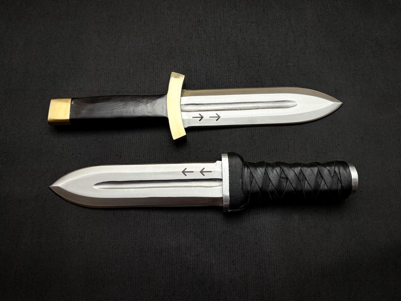 May include: Two daggers with silver blades and black handles are displayed against a dark background. One dagger has a gold crossguard and a black wooden handle with a gold end cap. The other has a black leather-wrapped handle.