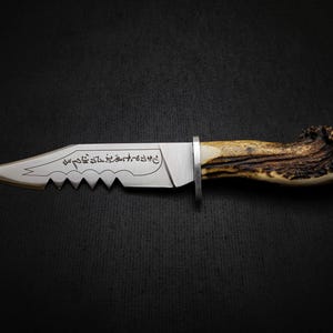 May include: A silver knife with a serrated blade and a brown antler handle. The blade is engraved with Arabic script.