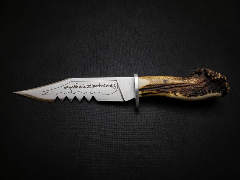 May include: A silver knife with a serrated blade and a brown antler handle. The blade is engraved with Arabic script.