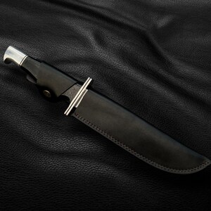 May include: A black leather knife sheath with a silver metal tip and a stitched edge.