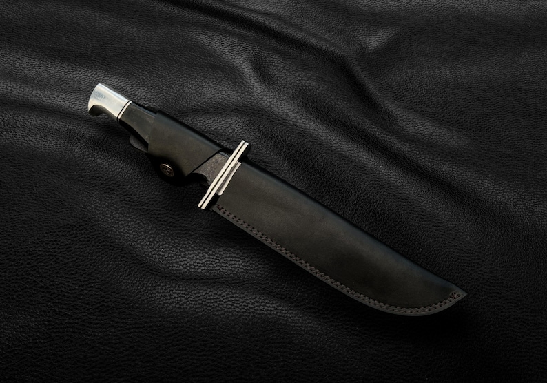 May include: A black leather knife sheath with a silver metal tip and a stitched edge.