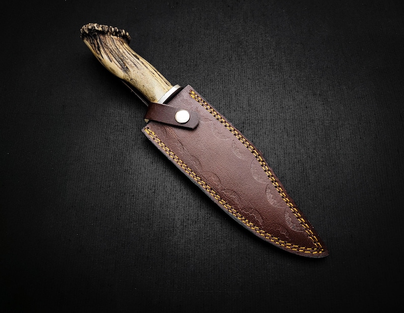 May include: A brown leather knife sheath with a decorative stitching pattern and an antler handle knife.