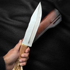 May include: A silver hunting knife with a brown leather sheath and a stag antler handle.