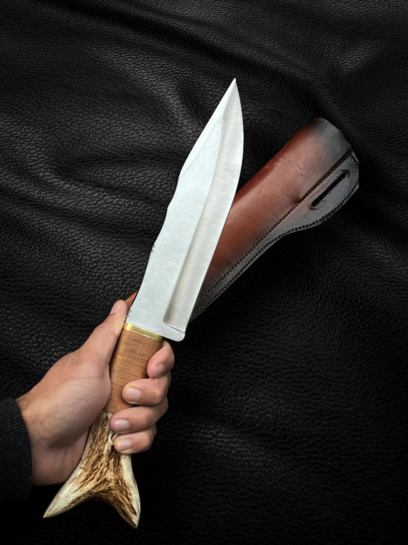May include: A silver hunting knife with a brown leather sheath and a stag antler handle.