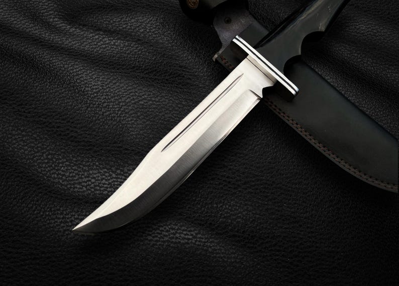 May include: A silver hunting knife with a black leather sheath. The knife has a long, sharp blade and a wooden handle.