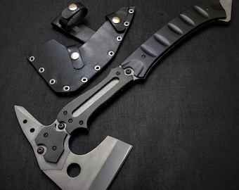 Puede incluir: Un tomahawk táctico con mango negro y hoja plateada, acompañado de una funda de cuero negro. El tomahawk presenta una cabeza de martillo y una hoja afilada, diseñada para diversas tareas al aire libre y de supervivencia.