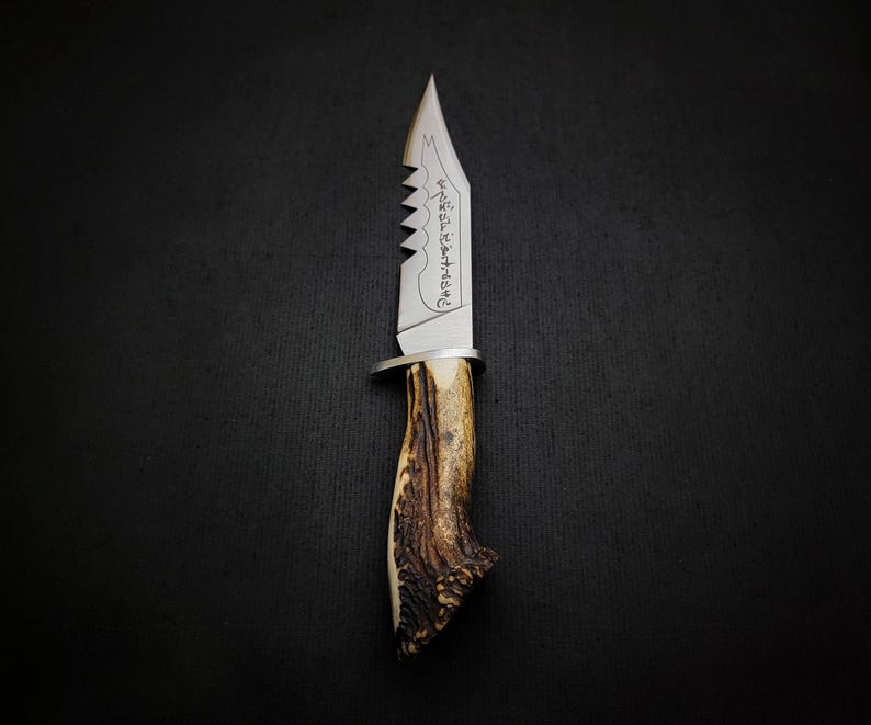 May include: A silver hunting knife with a serrated blade and a stag antler handle. The blade has an inscription that reads "Never Surrender".