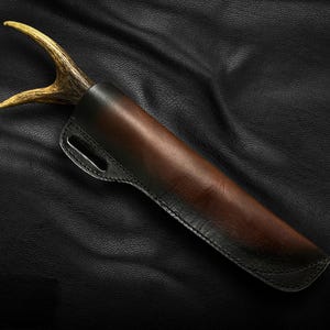 May include: A brown leather sheath with a black stitching detail and a light brown antler handle.