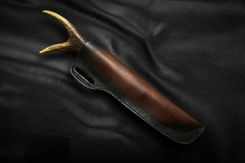 May include: A brown leather sheath with a black stitching detail and a light brown antler handle.