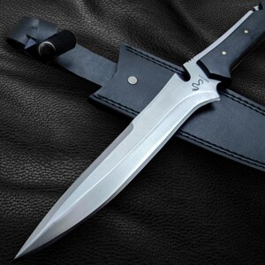 May include: A black leather sheath with a silver blade knife. The knife has a black handle with a silver inscription that reads "S.O.N."