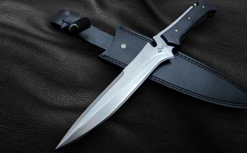 May include: A black leather sheath with a silver blade knife. The knife has a black handle with a silver inscription that reads "S.O.N."