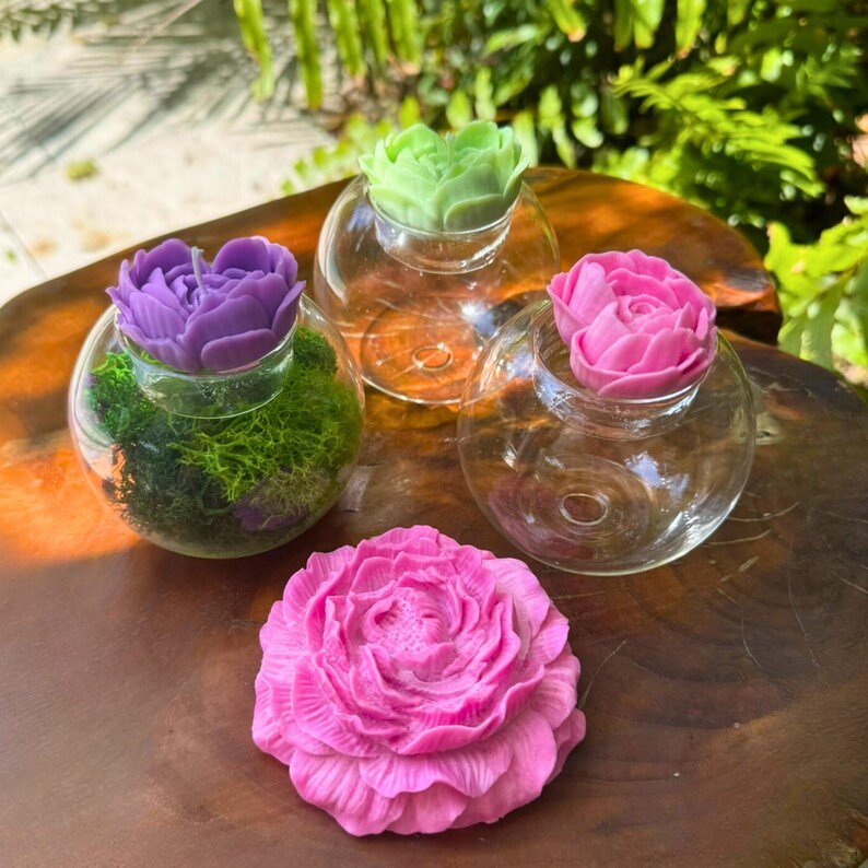 May include: A collection of decorative glass globes, each topped with a sculpted flower. One globe contains green moss and a purple flower, while others feature pink and green flowers. A large pink flower is also present.