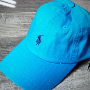 May include: A bright blue baseball cap with a small embroidered logo of a polo player on the front.