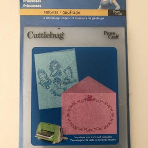 Może przedstawiać: Zestaw folderów do wytłaczania Cuttlebug Disney z motywem Kopciuszka. Zestaw zawiera dwa foldery do wytłaczania do tworzenia wzorów z motywem księżniczek. Opakowanie przedstawia różową kopertę i niebieską kartkę z sylwetkami księżniczek.