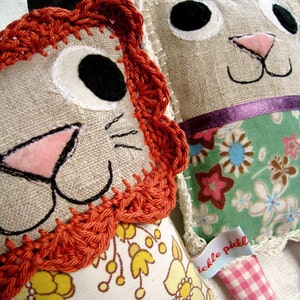 May include: Two handmade plush toys, one a lion with orange crocheted mane and a floral print, the other a white bunny with a green floral print and a pink gingham bow. The bunny has a tag that says "Tickle Pickle".