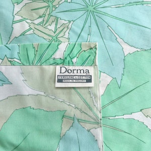 May include: A white fabric with a green and blue leaf pattern. The fabric has a label that reads "Dorma Regd. Terylene & Cotton Made in England."