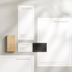Peut inclure: Maquette de présentation de marque professionnelle avec papeterie. L'ensemble comprend un bloc de bois, une carte de visite noire et du papier à lettres et blocs-notes blancs avec le texte "Sofia Marin Design Studio" et les coordonnées. Le design est minimaliste avec des lignes noires fines.