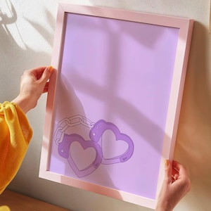 Könnte beinhalten: Ein gerahmter Druck mit helllila Hintergrund und einer Grafik von zwei lila herzförmigen Handschellen, die durch eine Kette verbunden sind.